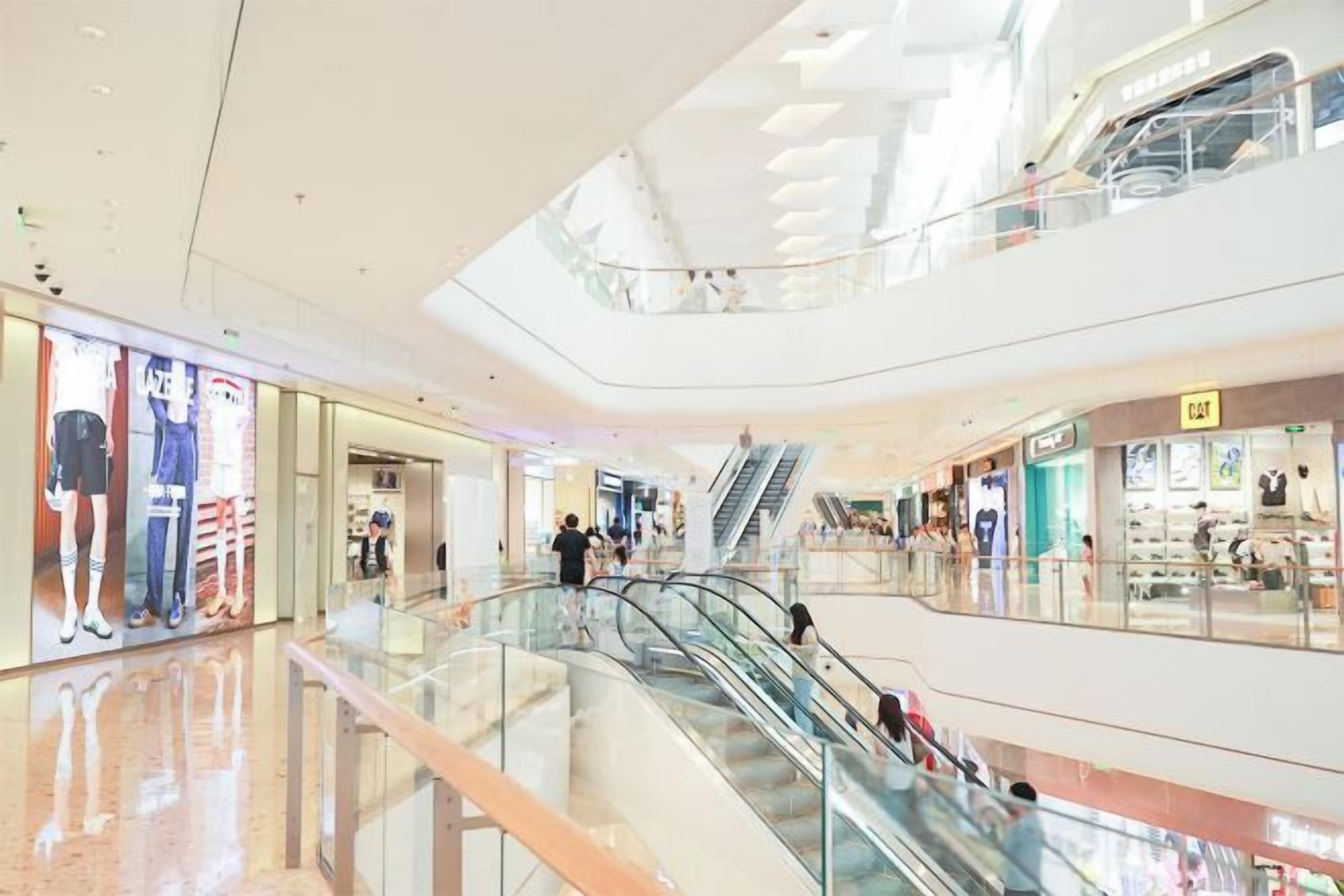 Et stort shoppingcenter med flere etager, rulletrapper, glasgelændere og mange butikker.