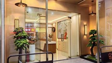 A hotel entrance with a reception desk, a glass door, and a small indoor plant.