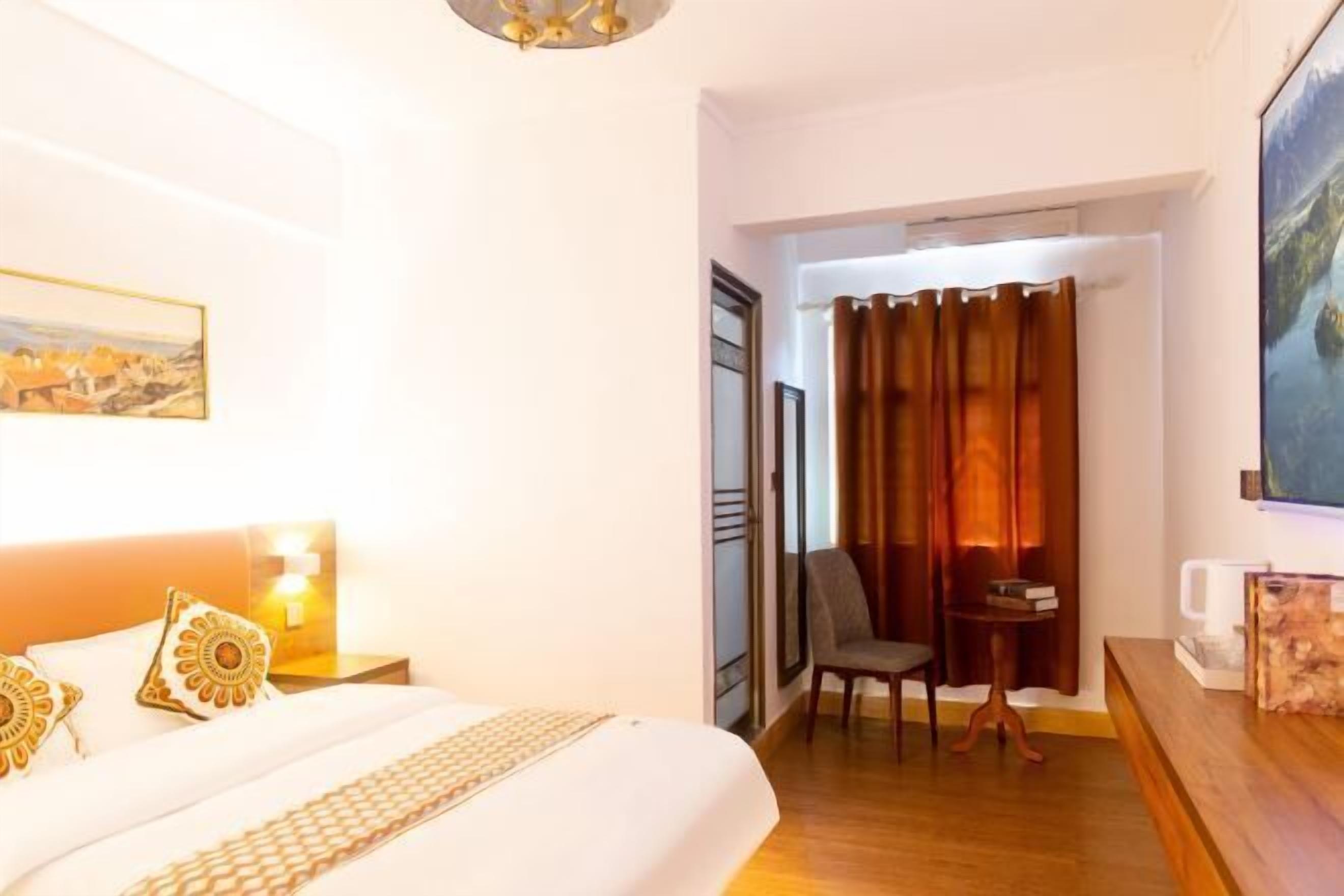 Una habitación de hotel con cama, una silla, una mesita, un cuadro y una cortina.
