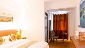 A hotel room with a bed, a chair, a small table, a painting, and a curtain.