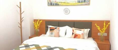 A neatly made bed with a patterned bedspread, two bedside tables with vases of yellow flowers, a wall-mounted picture frame, and a small wall-mounted air purifier.
