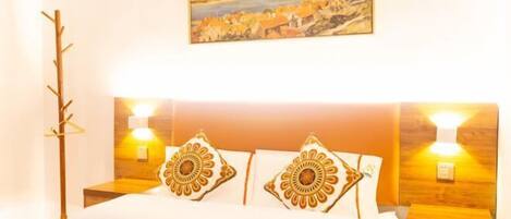 A neatly made bed with patterned pillows, a headboard with wall-mounted lights, and a painting above the bed.