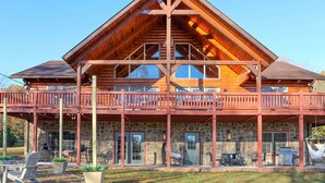 A large log cabin with a prominent front porch, stone foundation, and multiple windows. - Luxury, Curated Lakefront Cabin with New Hot Tub. Near Breweries and Vineyards! (Faber)