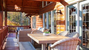 A wooden cabin with a porch, wicker furniture, and large windows. - Luxury, Curated Lakefront Cabin with New Hot Tub. Near Breweries and Vineyards! (Faber)