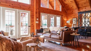 A cozy log cabin interior with a leather sofa, a coffee table, and a rustic rug. - Luxury, Curated Lakefront Cabin with New Hot Tub. Near Breweries and Vineyards! (Faber)