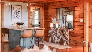 A wooden cabin interior with a kitchen area featuring a bar, stools, and a decorative tree stump table. - Luxury, Curated Lakefront Cabin with New Hot Tub. Near Breweries and Vineyards! (Faber)