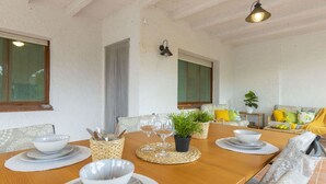 A dining area with a wooden table set for four, surrounded by cushioned chairs. There are woven placemats, a central potted plant, and a hanging light fixture above. - Stunning private villa for 9 guests with WIFI, A/C, private pool, TV, patio and pets allowed (Deltebre)
