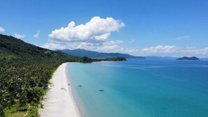 Uma praia com águas turquesa cristalinas, areia branca e colinas verdes exuberantes ao fundo.
