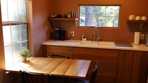 A compact kitchen with a wooden table and chairs, a sink, and a window with a view of trees.