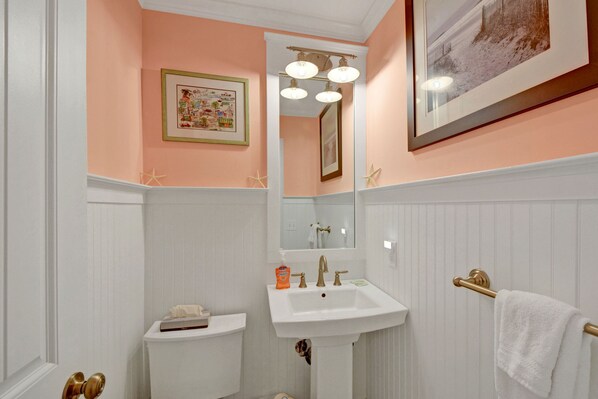 Een badkamer met een wit wastafelmeubel, een lijst met foto aan de muur, en een handdoekhouder.