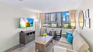 Ein modernes Hotelzimmer mit Fernseher, einer Sitzecke, einem Esstisch und einem Balkon mit Blick auf die Stadt.