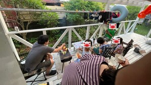 A covered outdoor area with a grill, seating, and a view of greenery.