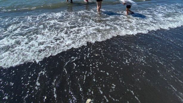 A beach scene with people walking and swimming in the water.