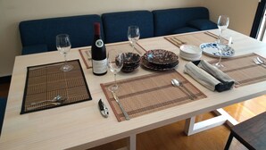 A dining table set with plates, cutlery, and wine glasses, with a sofa in the background.