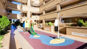 Un immeuble à plusieurs étages doté d’un espace de jeux pour enfants, comprenant un toboggan et des structures d’escalade.