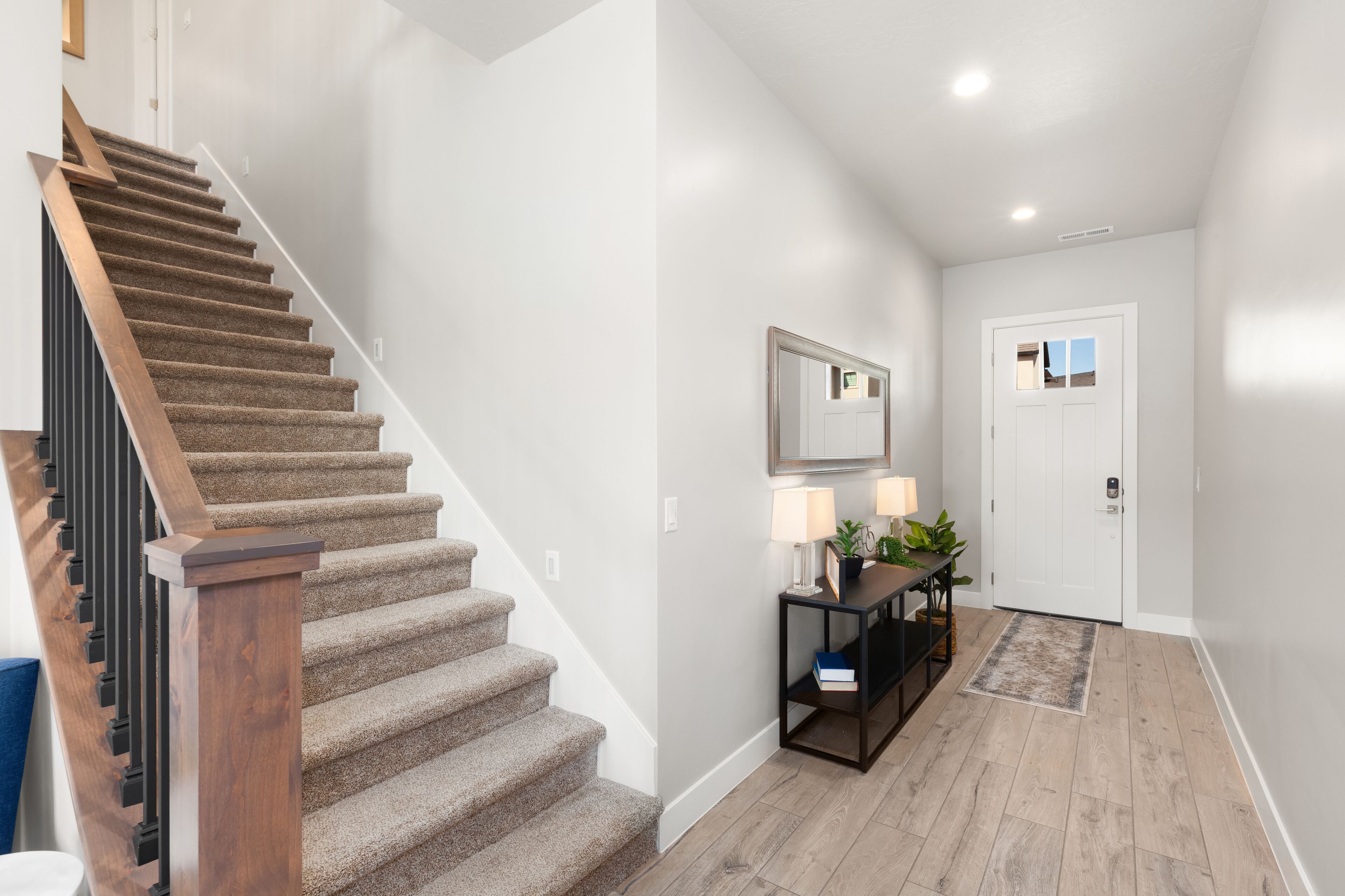 A staircase with wooden railings leading to a landing area with a console table, a mirror, and a door.