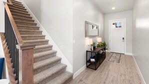 Una escalera con barandillas de madera que conduce a un rellano con una mesa consola, un espejo y una puerta.