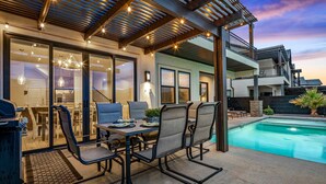 Un patio al aire libre con piscina, comedor y zona de estar techada.