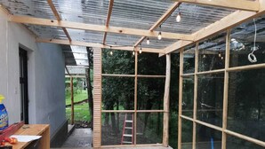 A room with a large glass window, a wooden ceiling, and a washing machine on the left. - Comfortable Cottage for Groups on 2 acre Homestead (San Jose Chacaya)