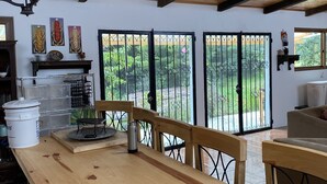 A spacious dining area with a wooden table and benches, a chandelier, and a view of a garden through large sliding doors. - Comfortable Cottage for Groups on 2 acre Homestead (San Jose Chacaya)