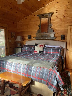 A wooden cabin bedroom with a bed, a nightstand, a lamp, a mirror, and a bench. - Cozy Cabin w/ great views, and close to Aska hiking trails!- Blue Ridge (Blue Ridge)
