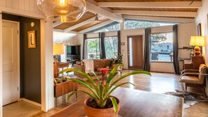 Een ruime woonkamer met een grote houten tafel, een potplant en uitzicht op de omgeving.