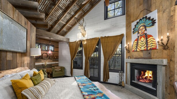 A rustic room with a bed, a fireplace, and a painting on the wall. - Agave | Fireplace | Outdoor Shower (Fredericksburg)