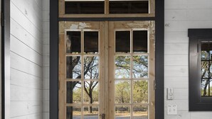 A wooden door with a black frame, white walls, and a small window to the right. - Agave | Fireplace | Outdoor Shower (Fredericksburg)