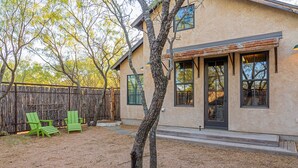 A house with a sandy yard, two green Adirondack chairs, and a wooden fence. - Agave | Fireplace | Outdoor Shower (Fredericksburg)
