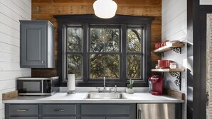 A kitchen with dark gray cabinets, a stainless steel sink, a microwave, and a red coffee maker. - Agave | Fireplace | Outdoor Shower (Fredericksburg)