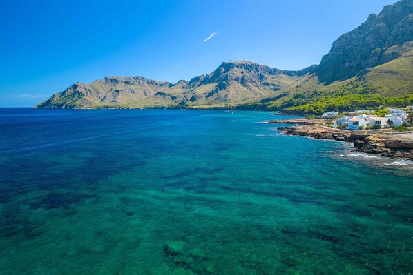A coastal area with clear blue waters, rocky shoreline, and white buildings with flat roofs.