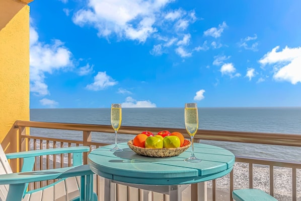 A table with a fruit bowl and two glasses of champagne, overlooking a body of water.