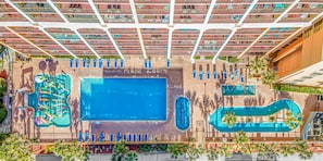 An aerial view of a hotel with multiple swimming pools, sun loungers, and a large library.