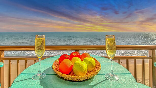 A table with a fruit basket and two glasses of champagne on a deck with a view of the sea and a sunset. - Caravelle 1414 (Myrtle Beach)