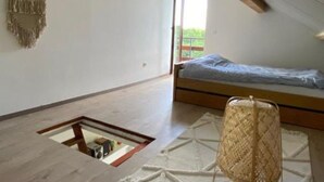 Una stanza piccola e luminosa con soffitto spiovente, un letto, un tavolino e un decorativo macramè appeso.