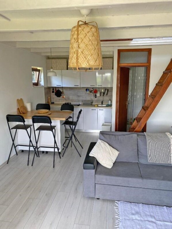 A compact living space with a kitchenette, a dining area with foldable chairs, a gray sofa, and a wooden staircase.