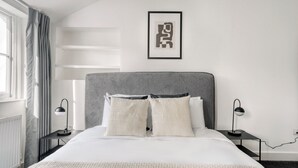 A modern hotel room with a large bed, two bedside tables, a headboard, and a framed artwork on the wall.