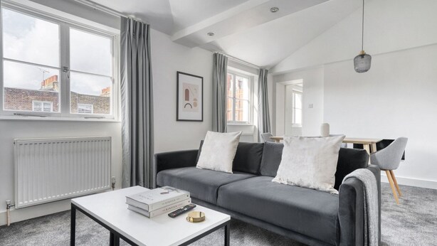 A modern living room with a grey sofa, a white coffee table, and a dining area with a table and chairs.