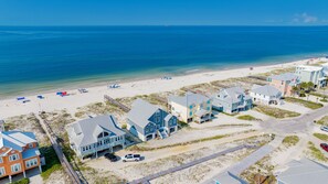 Zona residencial costera con propiedades frente al mar, un muelle y una playa con sombrillas.