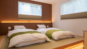 A modern bedroom with two beds, wooden flooring, and built-in lighting.