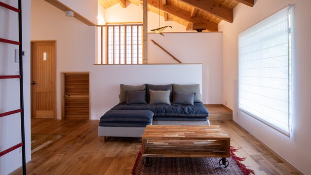 A modern living room with a wooden ceiling, a sectional sofa, a wooden coffee table, and a large window with blinds.