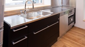 A modern kitchen with a stainless steel sink, a built-in oven, and a window overlooking the street.