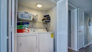 A laundry area with a washing machine, dryer, and stacked laundry. - Top Floor Oceanfront & Sound Views, Pool, (North Topsail Beach)
