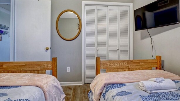 A bedroom with two wooden beds, a white wardrobe, a round mirror, and a television on the wall. - Top Floor Oceanfront & Sound Views, Pool, (North Topsail Beach)