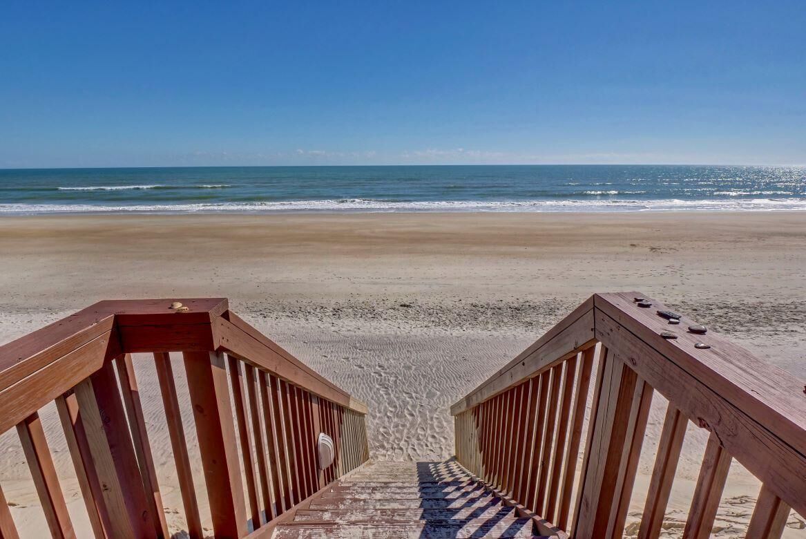 A wooden staircase leading to a beach with a clear view of the ocean.