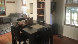 Een eetgedeelte met een donker houten tafel, twee stoelen en een decoratieve mand. Achtergrond toont een boekenkast met diverse objecten.