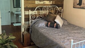 Een slaapkamer met een bed, een plafondventilator, een houten wand en een deur naar een badkamer.