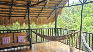 Un pontile in legno con tetto di paglia, un'amaca, una panchina con cuscini e una piscina gonfiabile rossa.