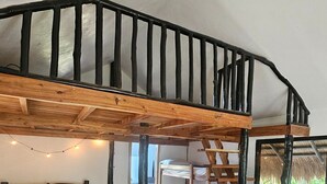 A loft bedroom with a wooden staircase, bunk beds, and a view through a window. - Mountainview Family Room Cabin (Binga)