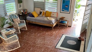 A spacious living area with a bed, wicker chairs, a small table, and a view of the outdoors. - Best Location, Caribbean views, Off street parking, walk everywhere. (Vieques)